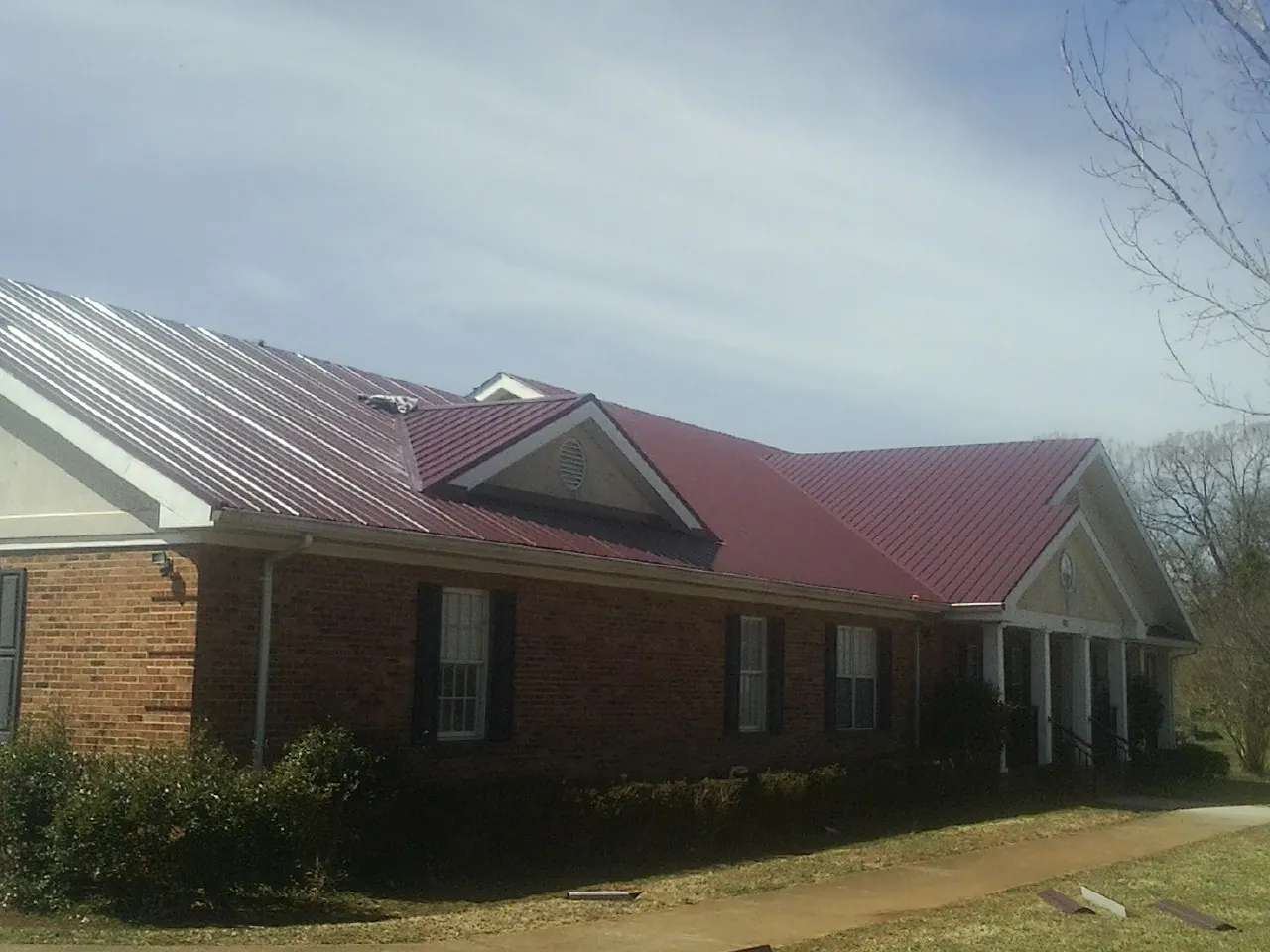 Red metal roof with gabled entries on a long brick building, from a Hail Damage Roof Repair job in Homedale
