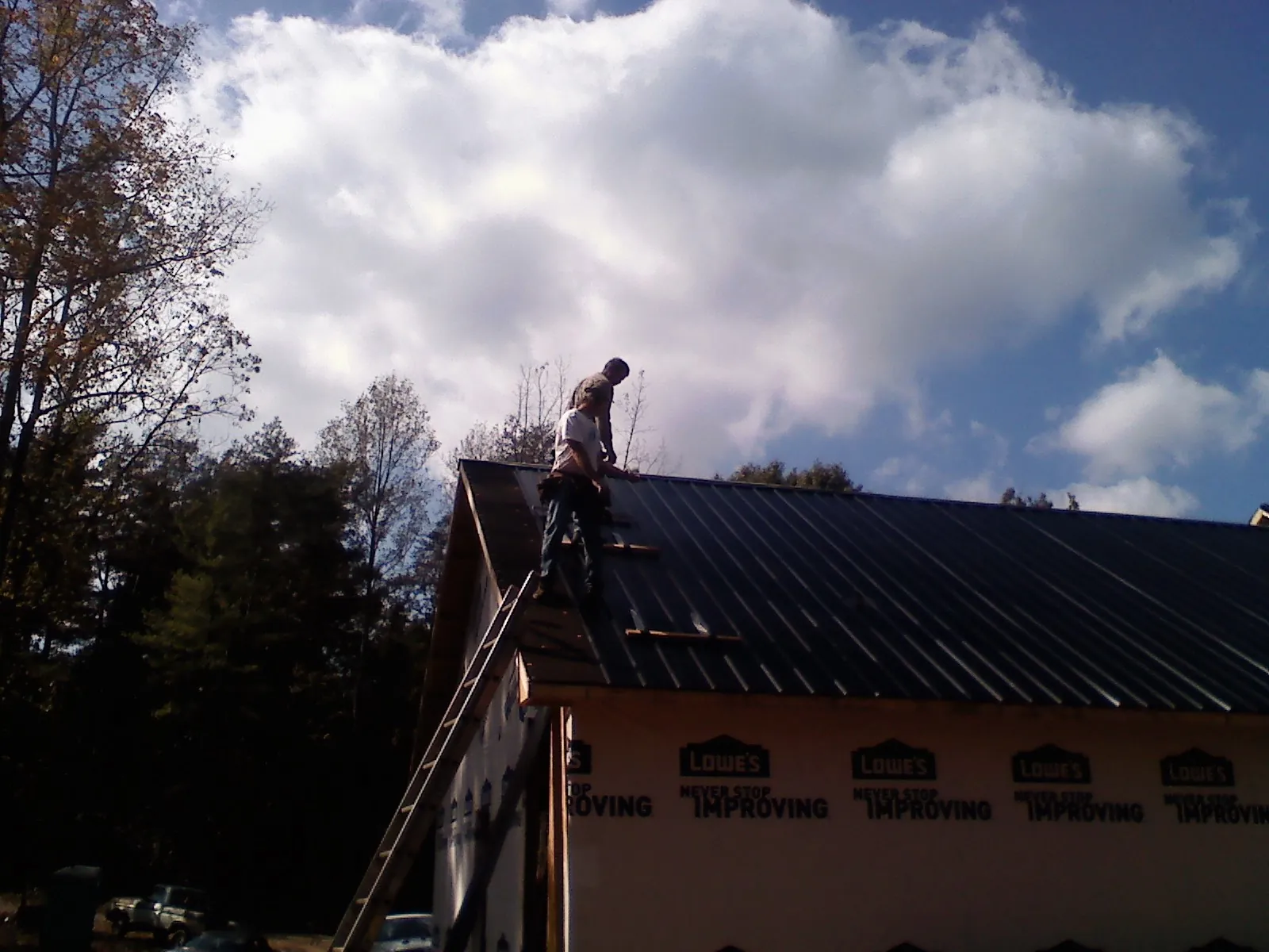Roofer fastening dark metal panels high against a cloudy sky, from a Roof Inspection job in Homedale