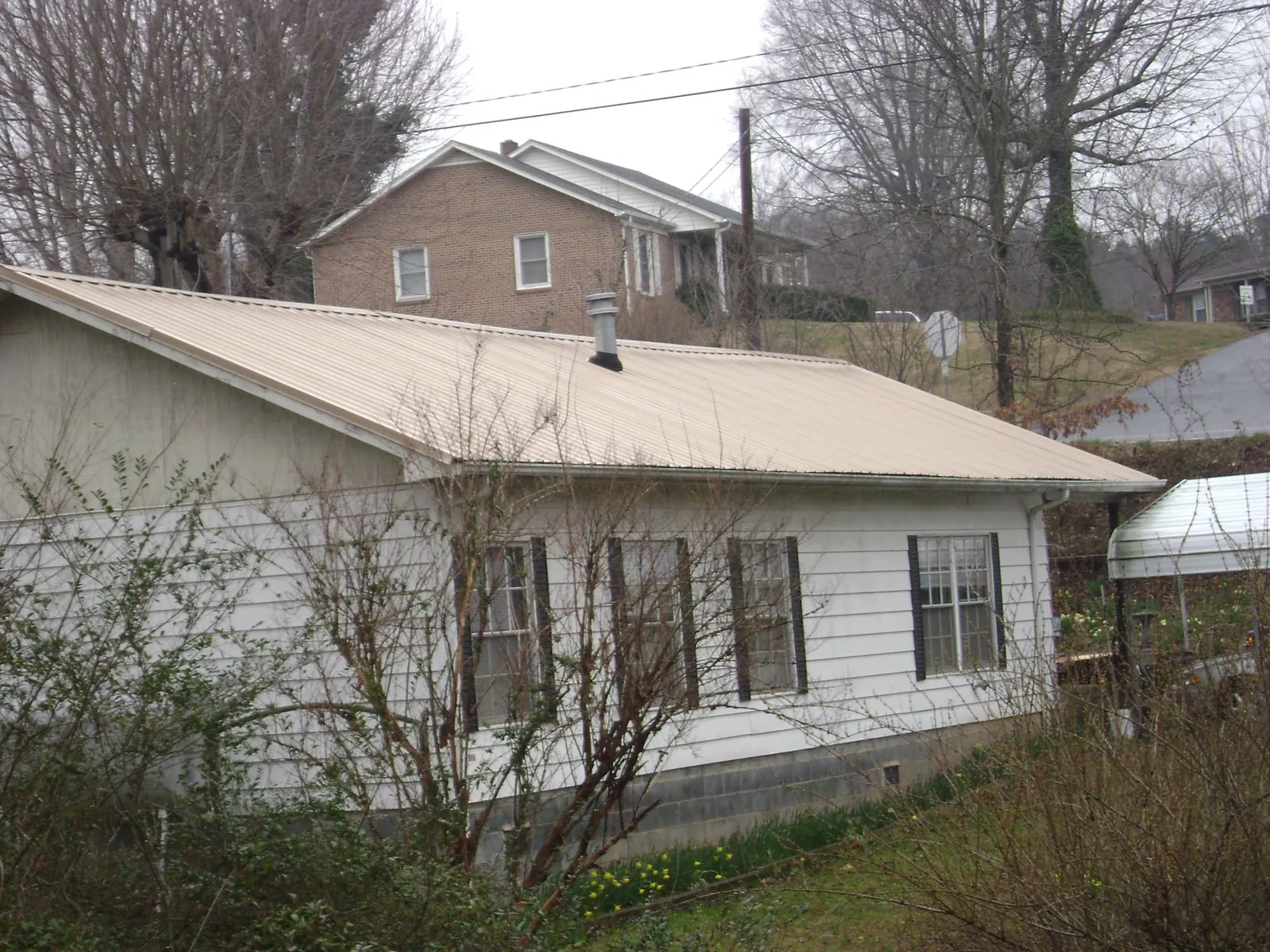 Tan metal roof on a white sided house set into a hillside — Commercial Roofing by Roofing Brothers in Homedale