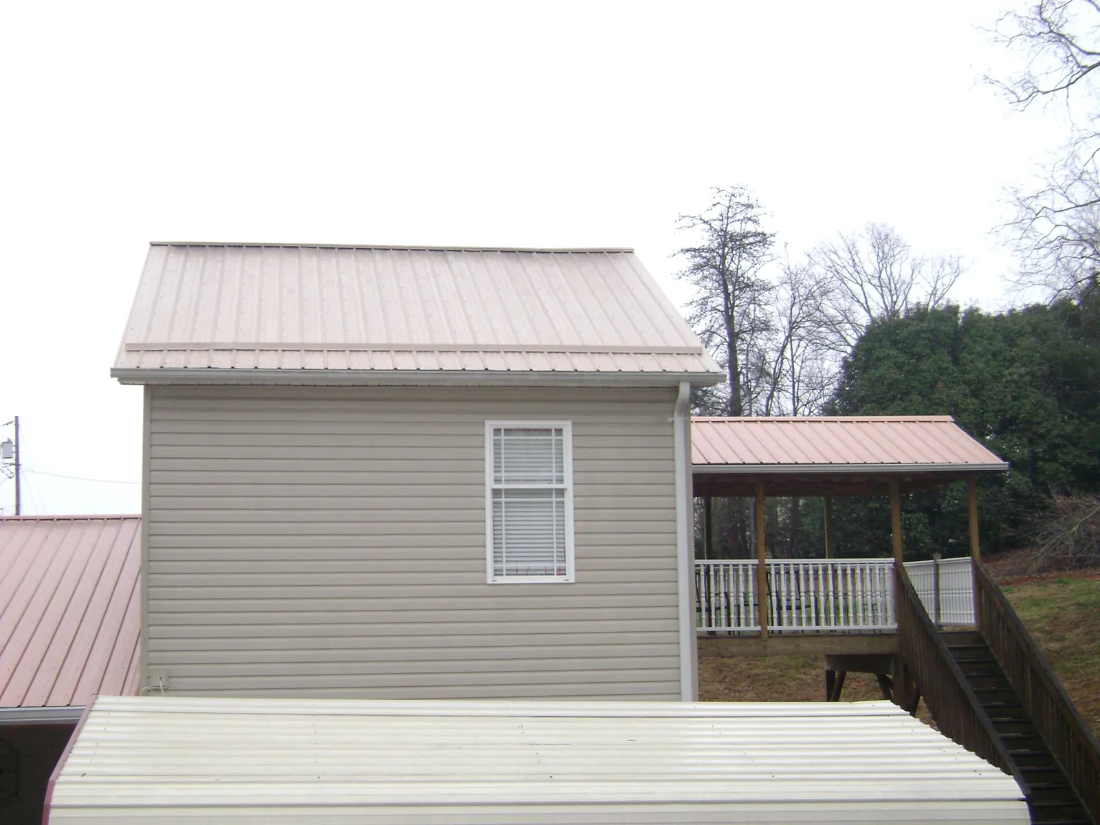 Tan metal roofs on a two story addition and attached porch, from a Roof Replacement job in Homedale
